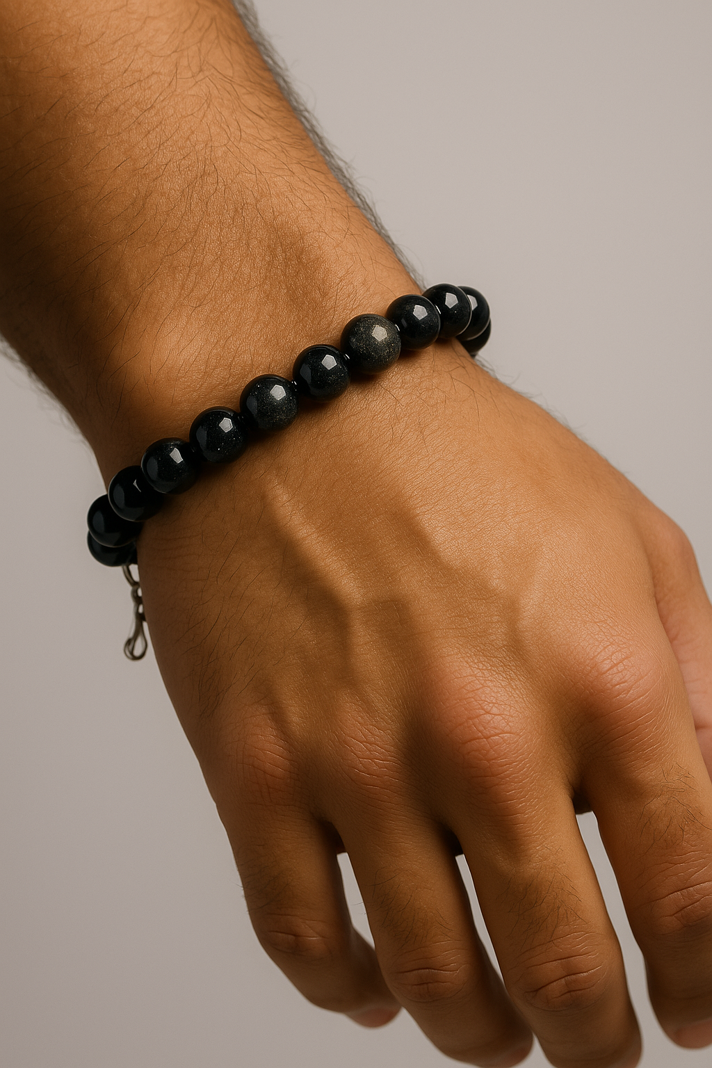 Black bead bracelet on man's wrist against neutral background